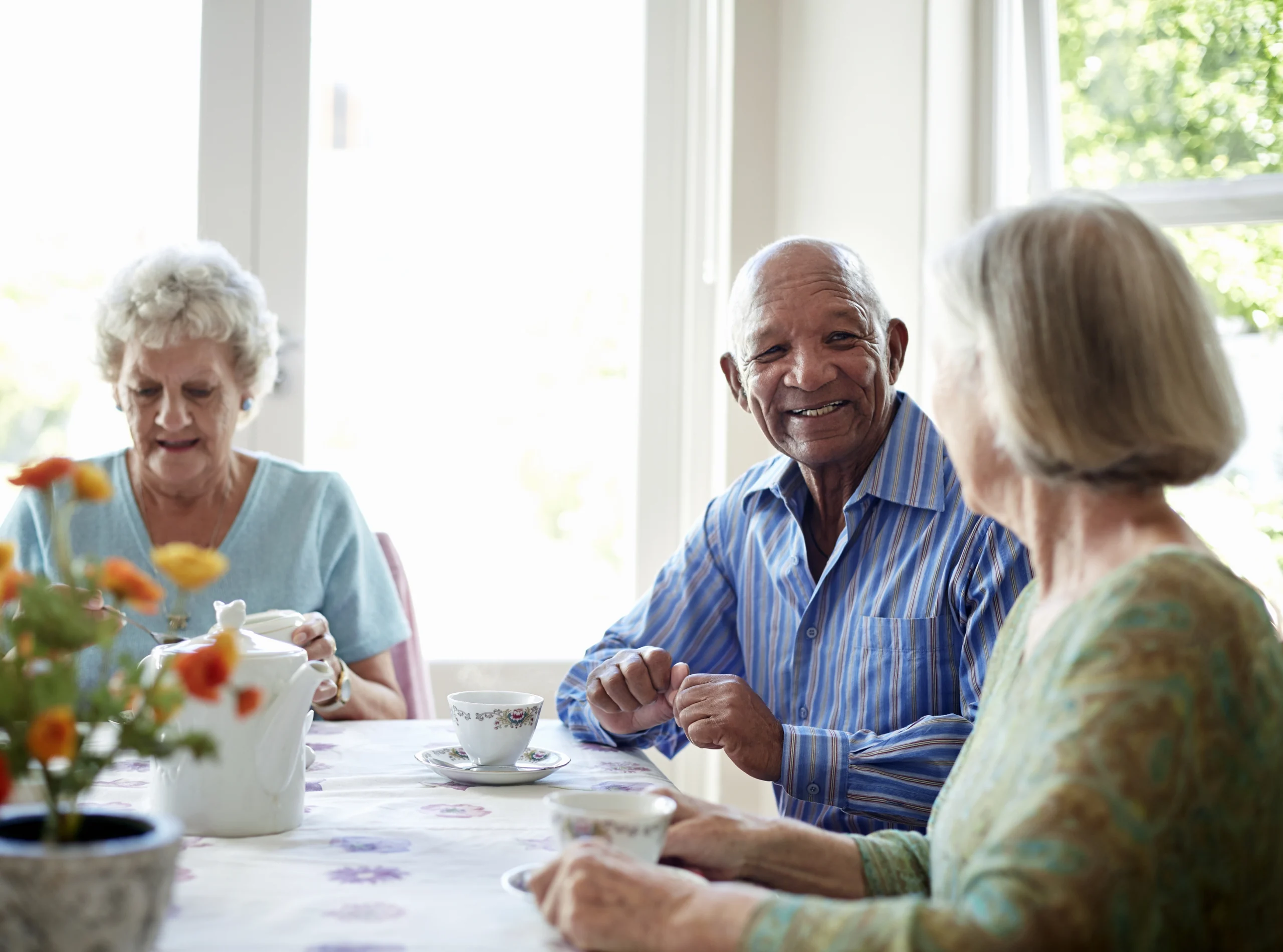 Group of three senior citizens, on man and two women, smiling and drinking tea