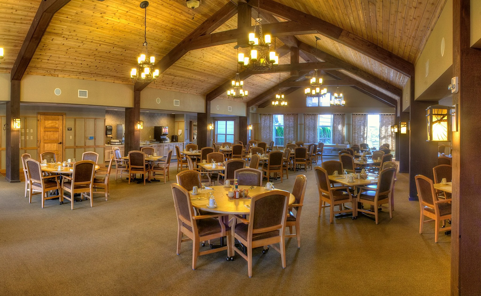 A large dining room filled with dozens of tables and lit by chandeliers hanging from the rafters