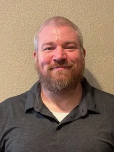 A smiling, heavyset middle aged man with a full brown beard