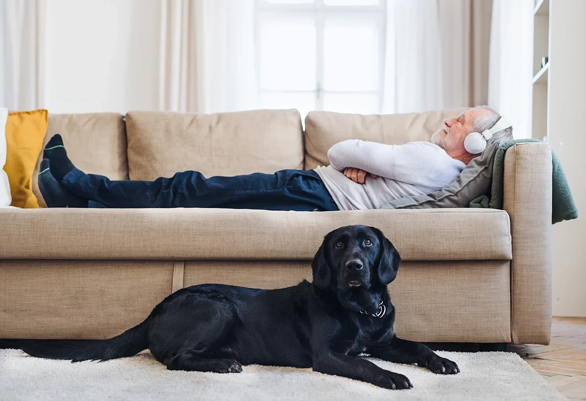 Elderly man lying on a sofa listening to music with his dog