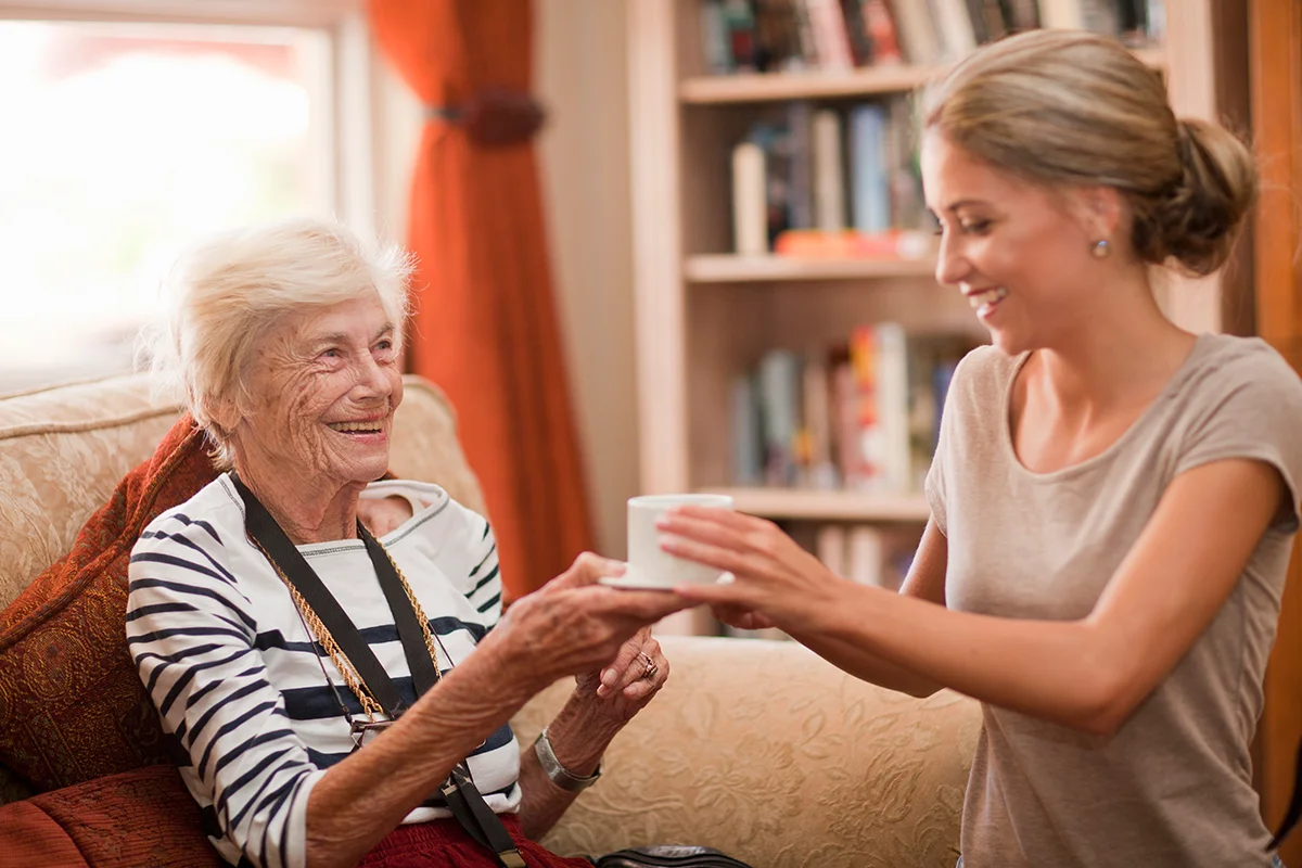 Care assistant giving happy senior woman a cup of coffee