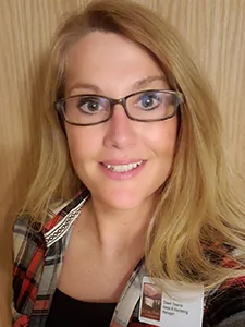 A smiling middle aged woman with glasses and blond hair