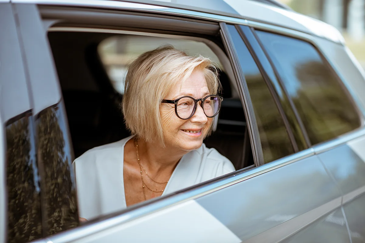 Elderly women with glasses smiling out of an open car window