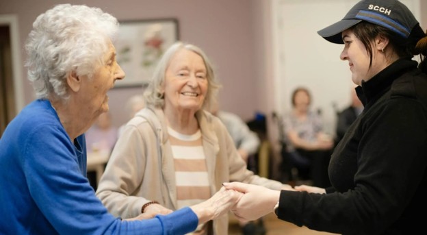 An elderly woman dancing with their caregiver in a senior living community.