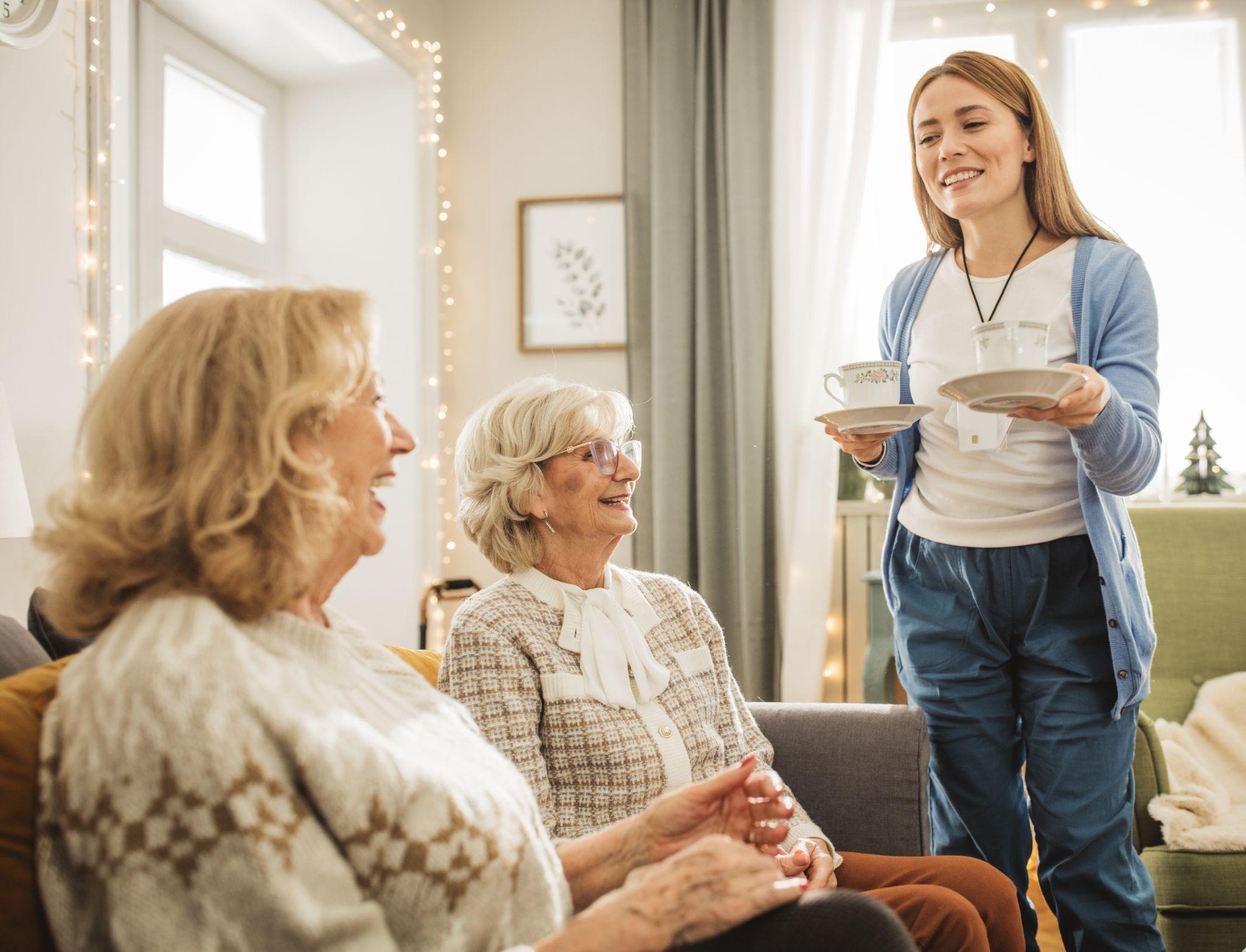 Caregiver serves tea to two older seniors in a memory care facility